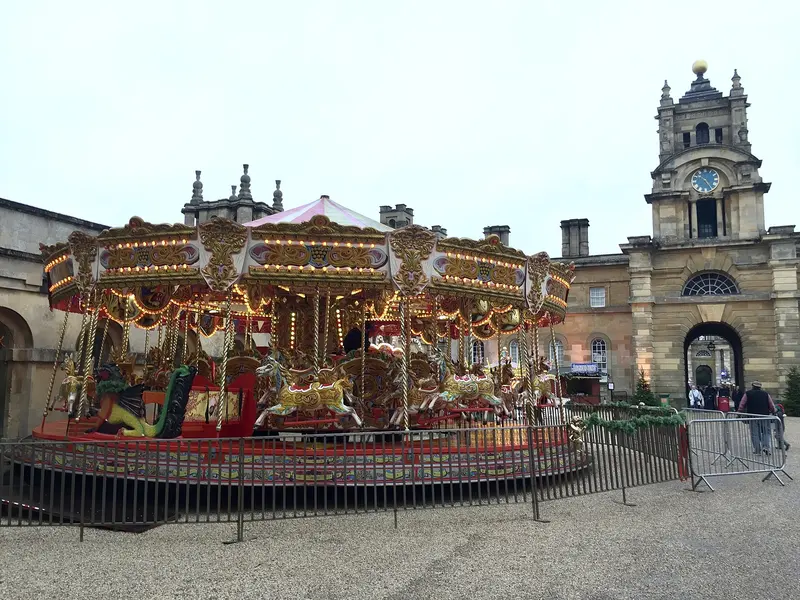A brightly painted carousel with gilded horses beneath the stone clock tower and archway of Blenheim Palace's courtyard