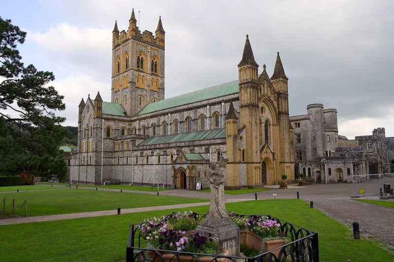 The pale stone abbey church at Buckfast, with its tall square tower and green copper roofs, behind lawns and a flower bed