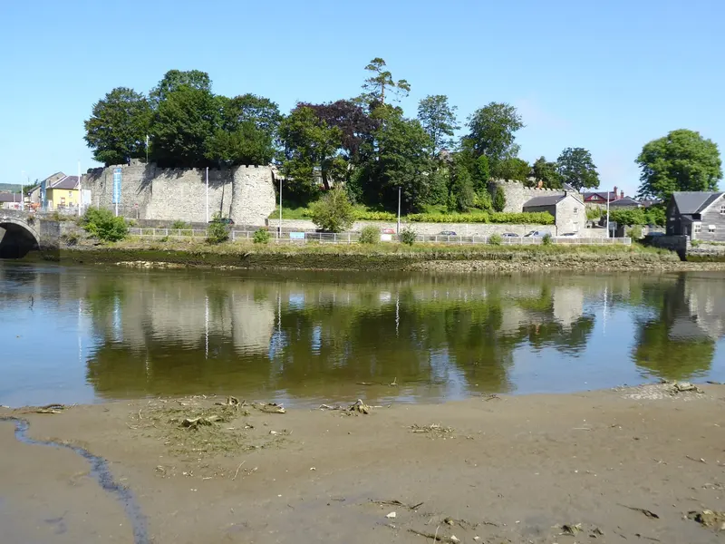 Cardigan Castle's stone walls and trees on a rise above the River Teifi, reflected in the still water at low tide
