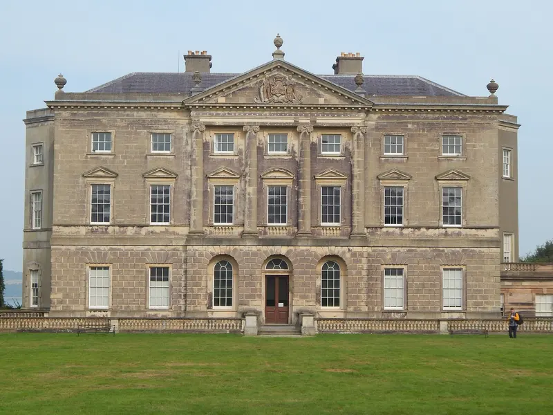 The pale stone classical front of Castle Ward house, with a central pediment and rows of sash windows, behind a lawn