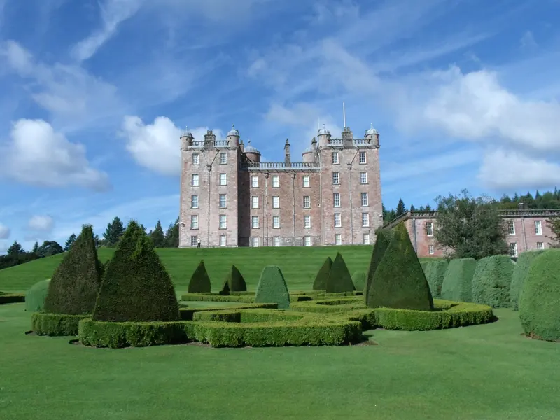 The pink sandstone towers of Drumlanrig Castle above clipped topiary cones and lawns under a blue sky