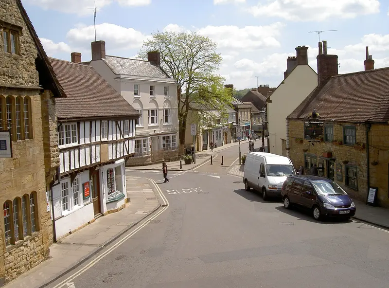 Sherborne's Cheap Street sloping downhill between golden-stone and timber-framed buildings, with a white van and a car parked by the kerb