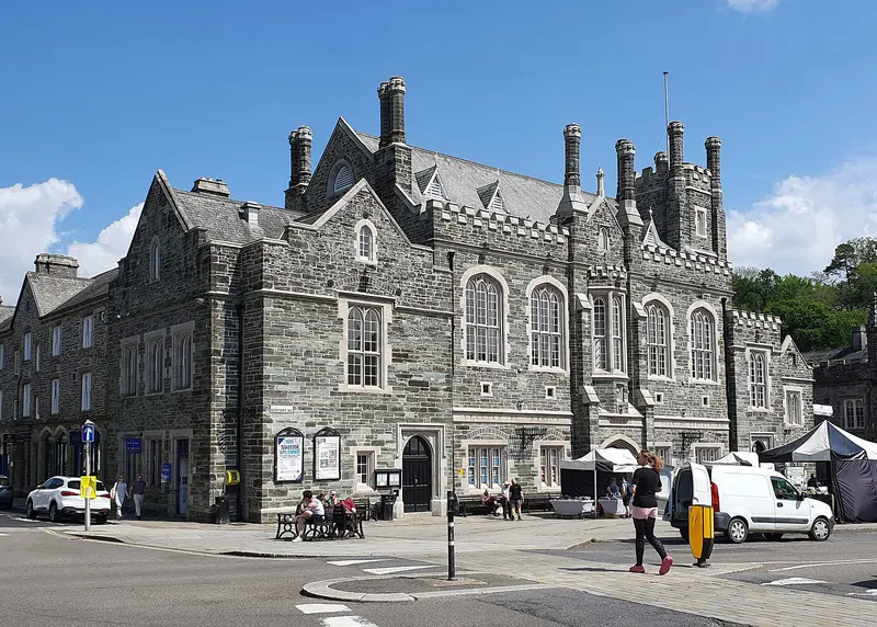Tavistock's grey stone Gothic-style Town Hall with tall chimneys and pointed windows on Bedford Square, under a bright blue sky