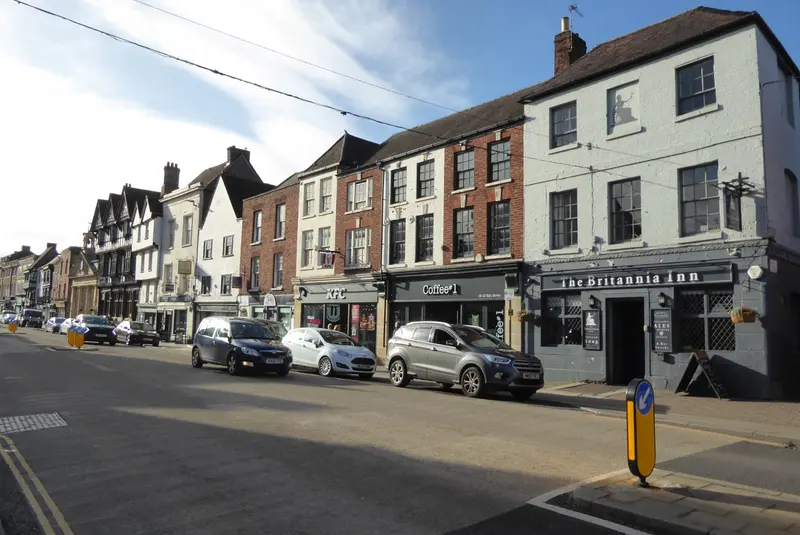 Tewkesbury High Street in low sunshine, a row of Georgian, brick and timber-framed buildings including the Britannia Inn, with cars parked outside